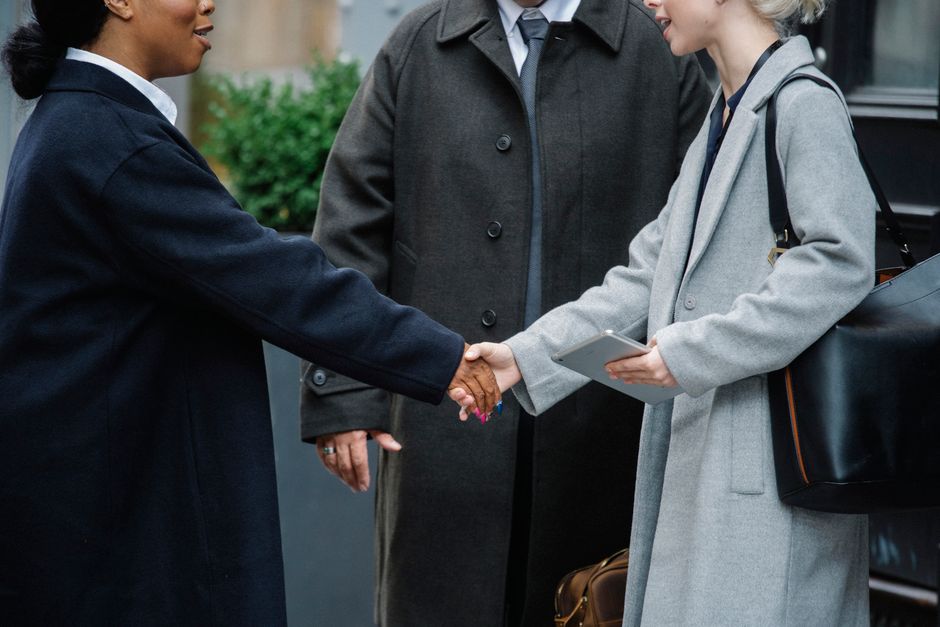 Crop anonymous diverse businesswomen in trendy elegant coats shaking hands after important conference on street