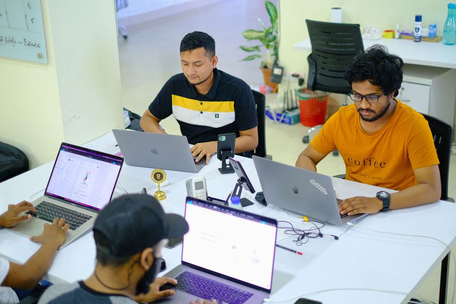 Team of Asian men working collaboratively in a modern office setting with laptops.