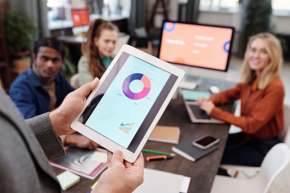 Business team using a tablet to analyze digital marketing data with charts in an office setting.